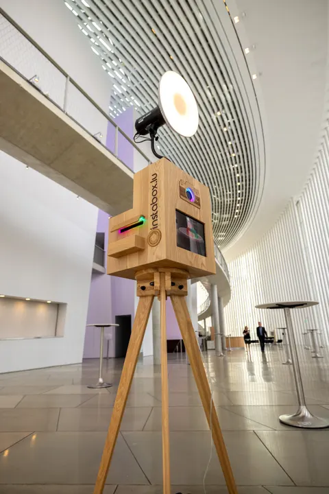 Fotobox aus Eiche mit Studiolicht auf einem Holzstativ in einer modernen Halle mit geschwungener weißer Lamellendecke