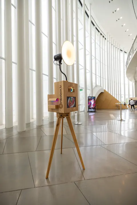L’Instabox W en chêne sur son trépied, lampe allumée, seule dans le foyer de la Philharmonie Luxembourg aux hautes colonnes blanches, avant l’arrivée des invités