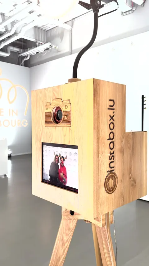 Nahaufnahme einer Fotobox aus Eiche mit Kamerasymbol und Touchscreen mit frischem Foto in einem weißen Ausstellungsraum