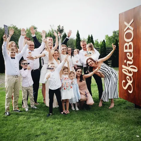 Fotobox-Foto: Große Familiengruppe jubelt mit erhobenen Armen auf einer Wiese, die Kinder vorne, bei einem Sommerfest