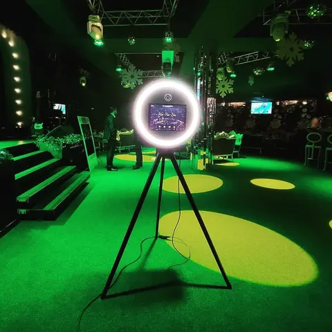 Fotobox mit Ringlicht auf einem Stativ in einer dunklen Location mit grünen Strahlern und Lichtmustern auf dem Boden