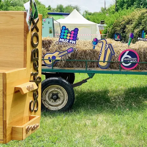 Holz-Fotobox im Freien neben einem Heuwagen mit Musik-Ausschnitten als Deko auf einem Sommerfestival