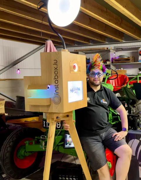L’animateur lors d’un événement, perruque arc-en-ciel et lunettes rigolotes, à côté du photobooth Instabox W en chêne