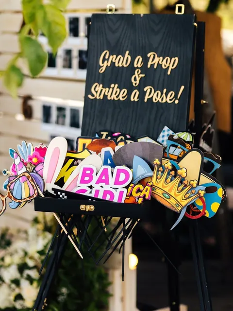 Un panneau « Grab a Prop & Strike a Pose! » au-dessus d’une mallette d’accessoires photobooth colorés : couronne, lunettes, oreilles de lapin et pancartes